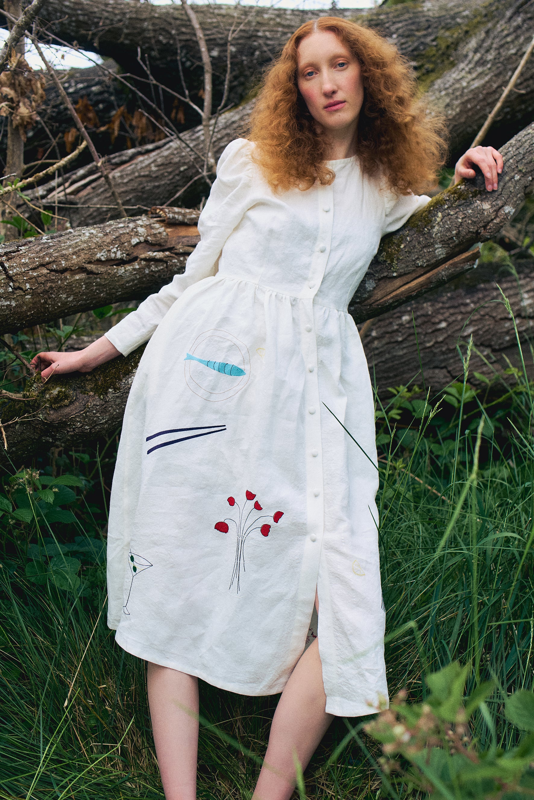Cream Irish linen dress with long sleeve, cover buttons along the centre front and a midi length skirt. Colourful embroidery of cutlery, prawns, fish and flowers  